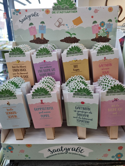 Ein Display mit bunten Saatgut-Packungen der Marke "Die Stadtgärtner", verziert mit humorvollen Sprüchen.