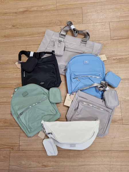 Verschiedene Taschen und Accessoires in gedeckten Farben auf Holzboden, ordentlich arrangiert.