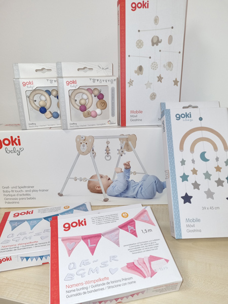 Sammlung von goki Babyspielzeug in sanften Farben, darunter Spieltrapez, Mobiles und Rasseln.