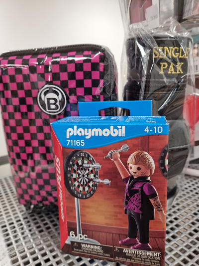 Nahaufnahme von Playmobil-Set, karierter Tasche und "Single Pak" auf metallischer Oberfläche.